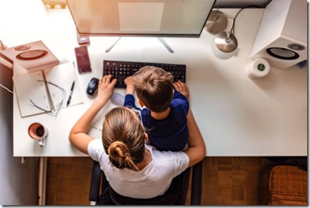 Overhead view of young mother working on computer with her son sitting in her lap during the day.