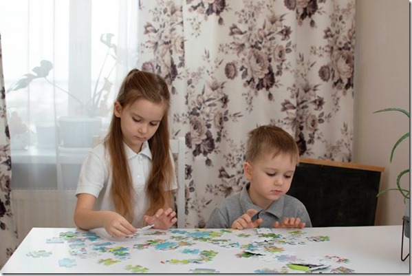 Boy and a girl are assembling a puzzle on the table. The child collects the puzzle pieces to make a picture. Development of mind, skills, understanding, games, pastime. Selective focus.