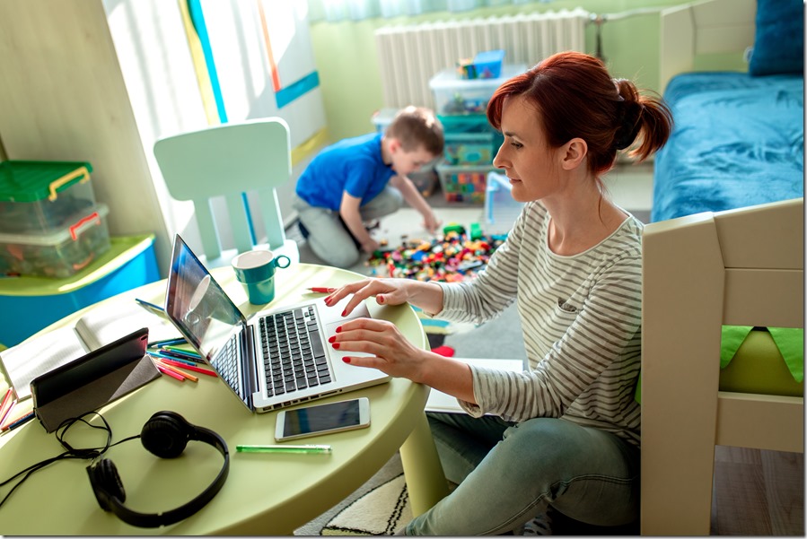 Mother working remotely on laptop while taking care of her son playing with toys in his room.