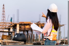 Construction Engineering Asian woman civil engineer paper plan building architect wearing white safety helmet look at the construction site.