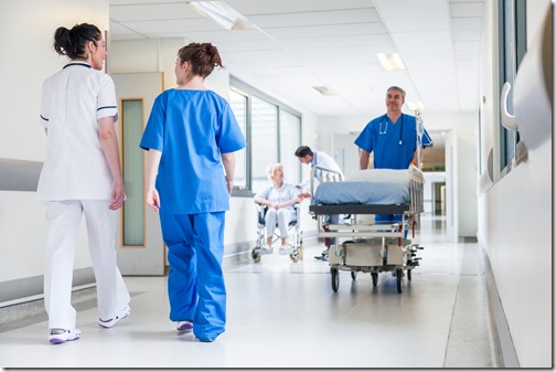 Male nurse pushing stretcher gurney bed in hospital corridor with doctors & senior female patient