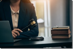 Beautiful young woman lawyer sitting in front of laptop in room with documents and smartphone with empty hammer and scale next to it justice and legal concept