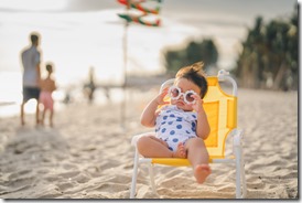 baby in white dress and sunglasses sit on the chair beach yellow color with relaxing and the wind blows in evening time and beautiful sunset light