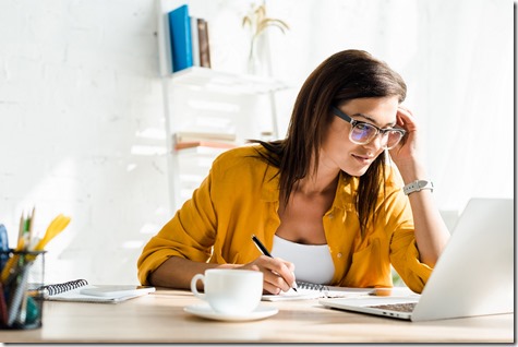 attractive female freelancer working on laptop and writing in home office