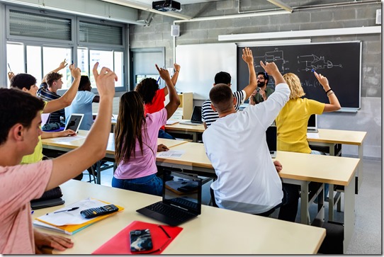 Group of high school students raising hands in classroom