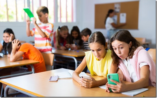 Schoolchildren use mobile phones at the lesson in classroom