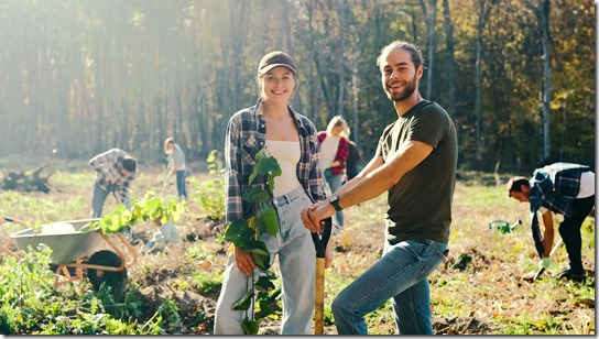 Portrait of young Caucasian happy couple of eco activists smiling to camera in park on sunny day and planing seedling of tree on field in forest or park. Outdors. Handsome man and pretty woman.