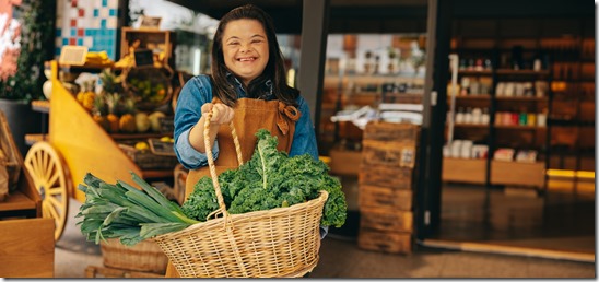 Grocery store employee with down syndrome holding a basket of fresh vegetables