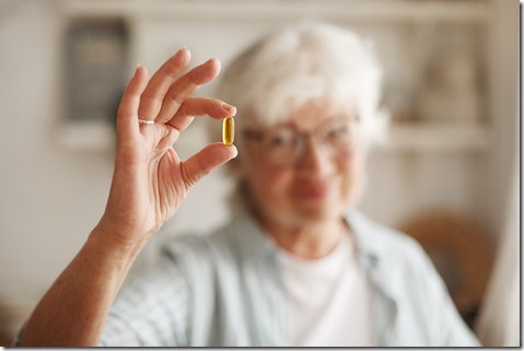 Food, nutrition, diet and health concept. Close up shot of elderly woman's hand holding fish oil or omega-3 polyunsaturated fatty acid supplement in shape of capsule, going to take one during lunch