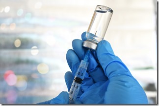 Medical personnel filling a syringe needle with generic vaccine booster from vial