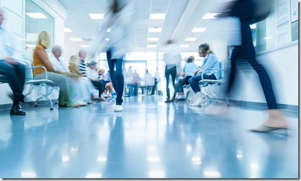 A busy hospital waiting area with patients sitting in chairs and blurred medical staff walking through the corridor, capturing the hustle of a healthcare environment